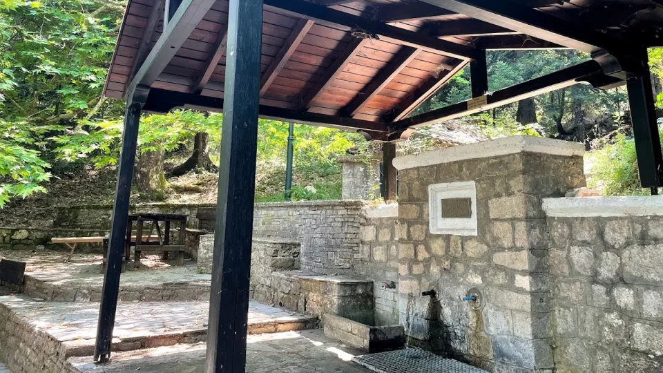 Πέτρινη βρύση με ξύλινο στέγαστρο και πάγκους μέσα στο δάσος