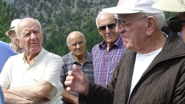 Ο Βασίλης Γκανάτσιος συζητά με ηλικιωμένους άνδρες σε εξωτερικό χώρο